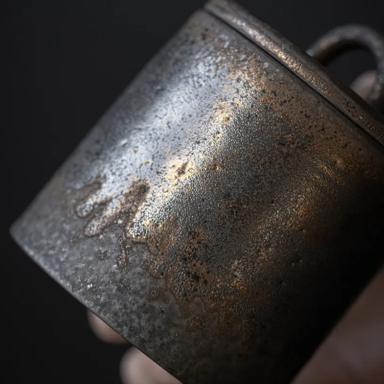 Closeup of dark grey ceramic storage jar with bronze accents on dark neutral background