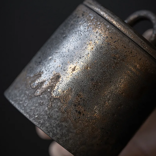 Closeup of dark grey ceramic storage jar with bronze accents on dark neutral background