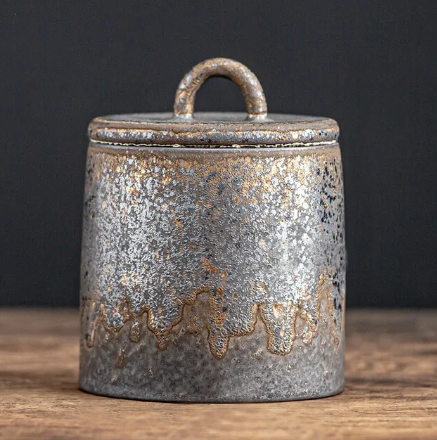 Dark grey ceramic storage jar with bronze accents on dark neutral background