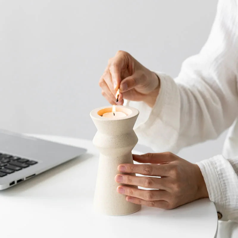 Hands lighting tealight in white ceramic candle holder on light neutral background