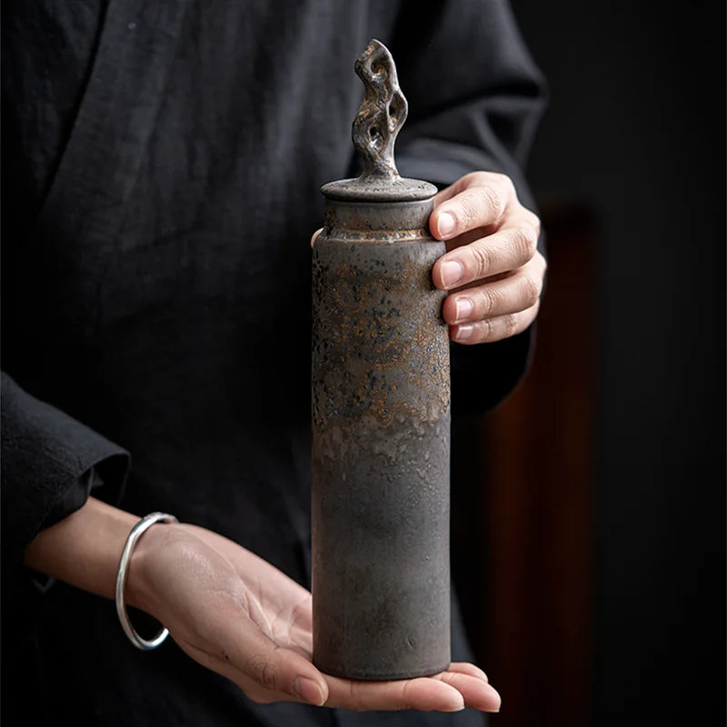 Hands holding tall, dark grey ceramic storage jar with bronze accents