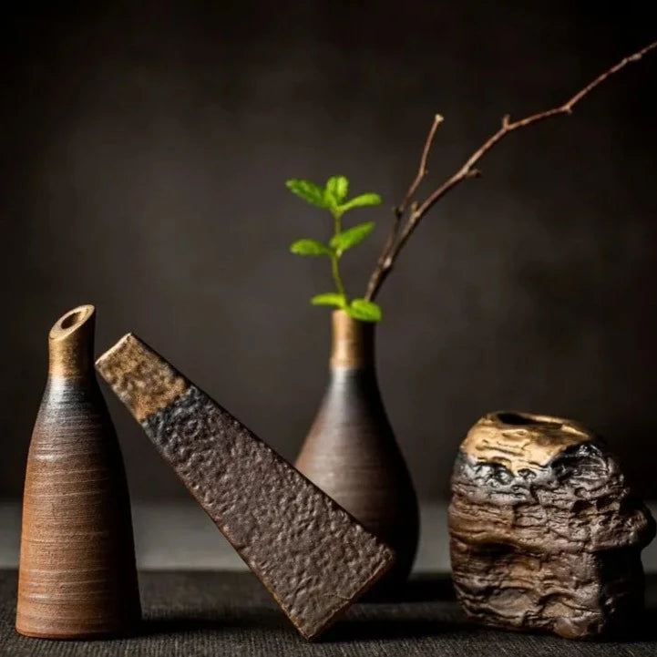 Composition of dark grey textured ceramic vases with bronze accents and different shapes, on dark neutral background