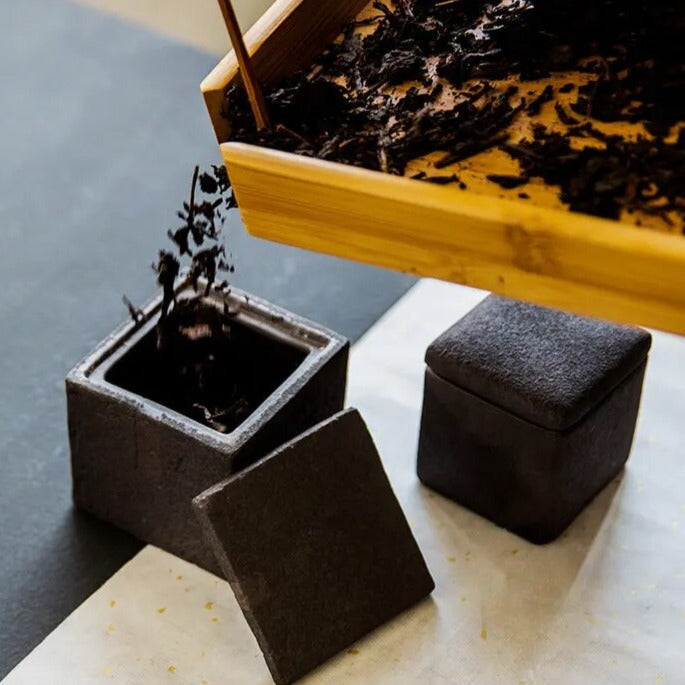 Pouring tea into dark grey textured square ceramic jar