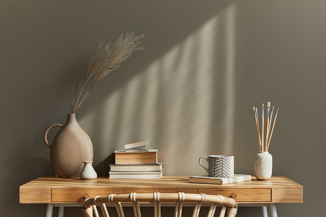 Wooden table with books, vases and mug, bamboo chair and beautiful calming lighting from window in neutral color room