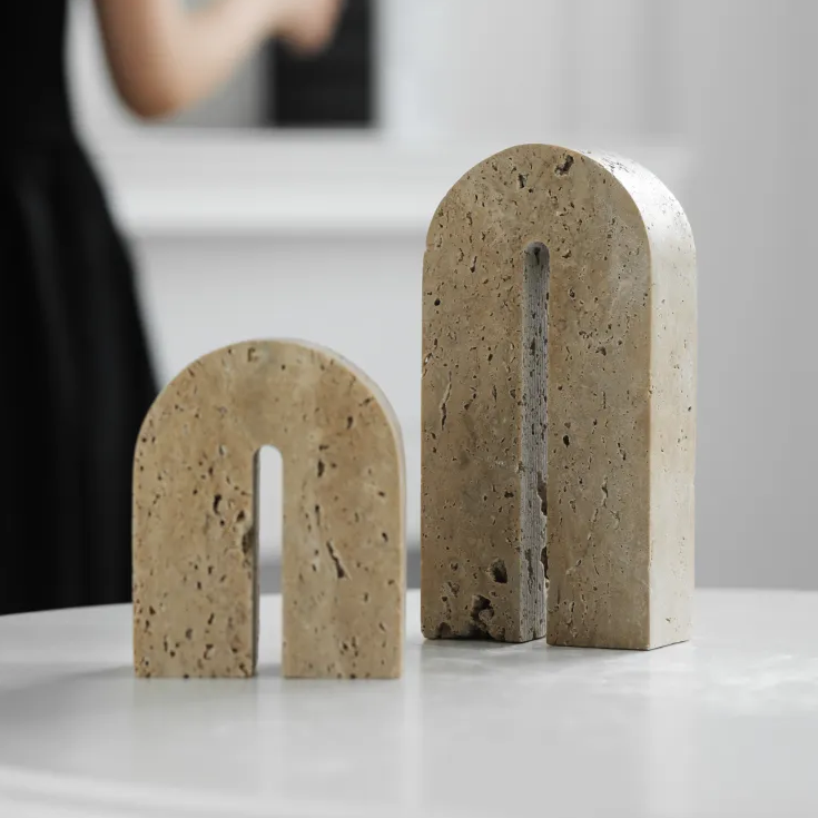 A set of two handcrafted, arch shaped travertine book ends in room with woman