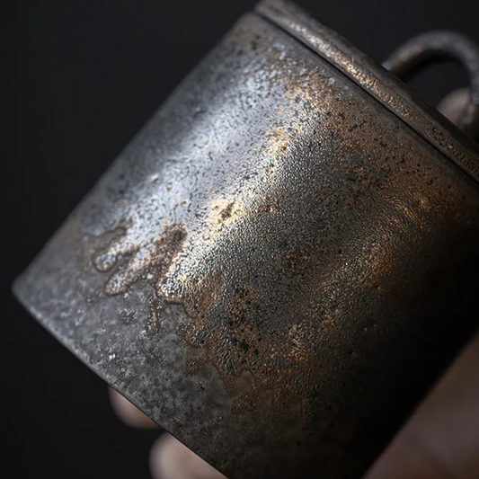 Closeup of dark grey ceramic storage jar with bronze accents on dark neutral background
