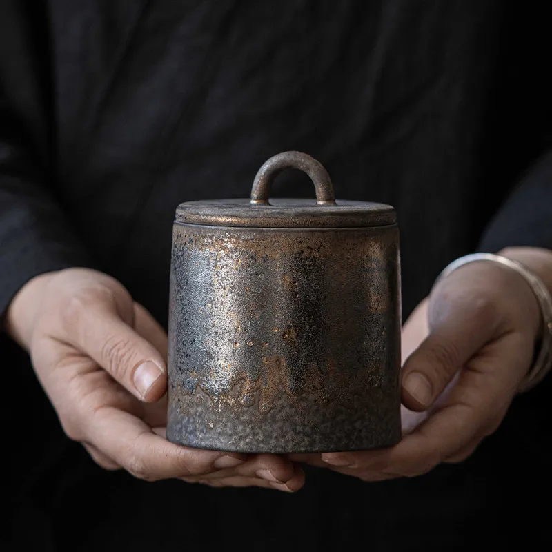 Hands holding dark grey ceramic storage jar with bronze accents 