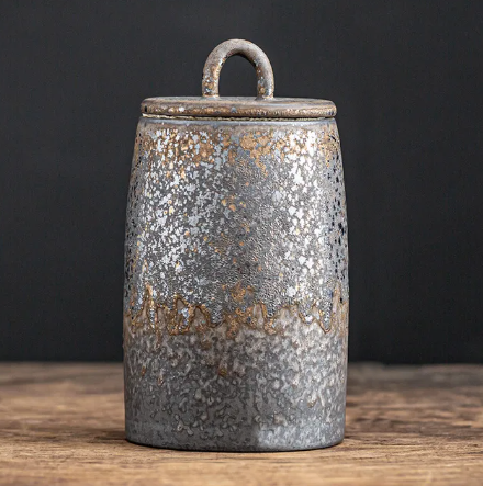 Dark grey ceramic storage jar with bronze accents on dark neutral background