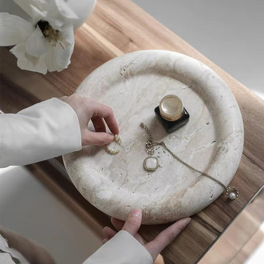 Woman’s hands displaying jewelry on round marble tray, with neutral colors in japandi room