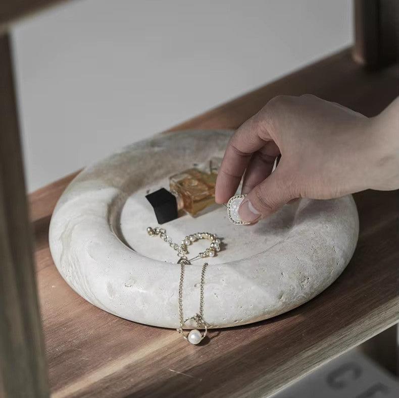 Woman’s hands displaying jewelry on round marble tray, with neutral colors in japandi room