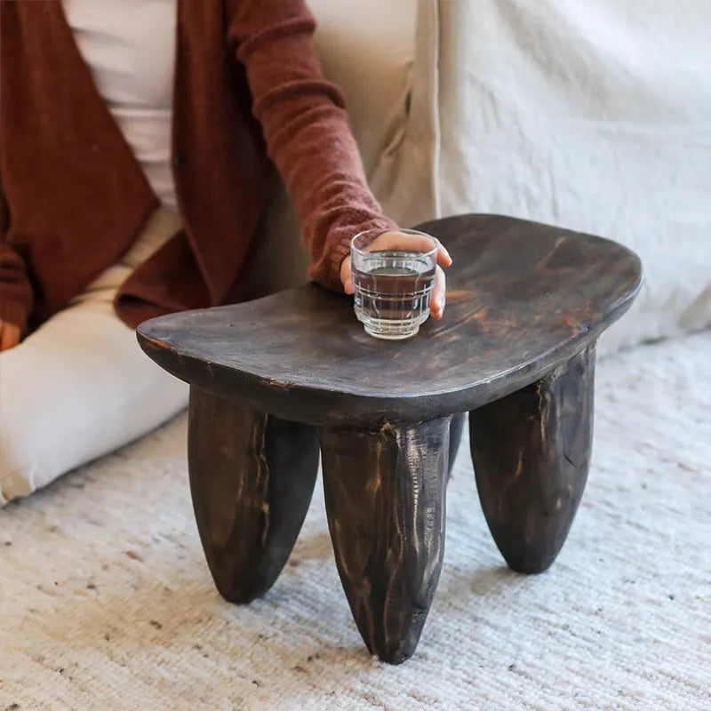 Hand holding a glass over Japandi wooden stool in neutral room