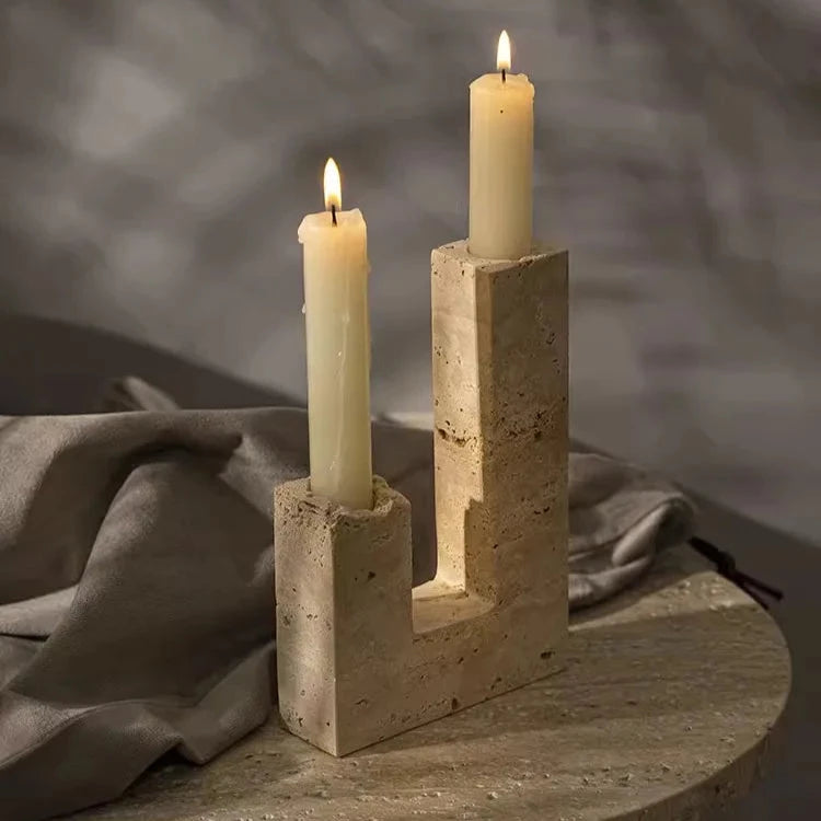 Handcrafted travertine candle holder with two burning candles on marble table