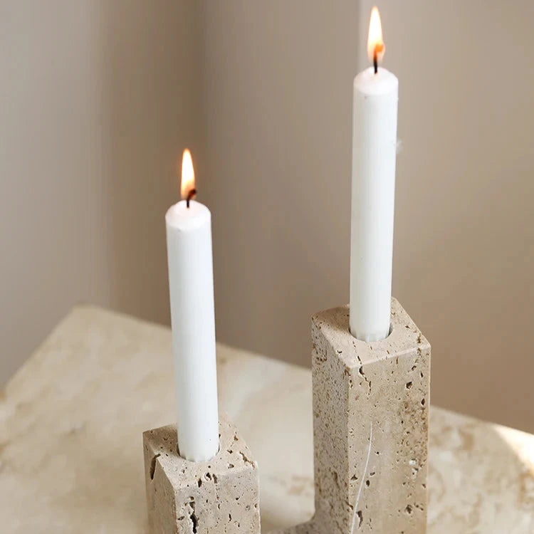 Handcrafted travertine candle holder with two white candles on table, and neutral room background