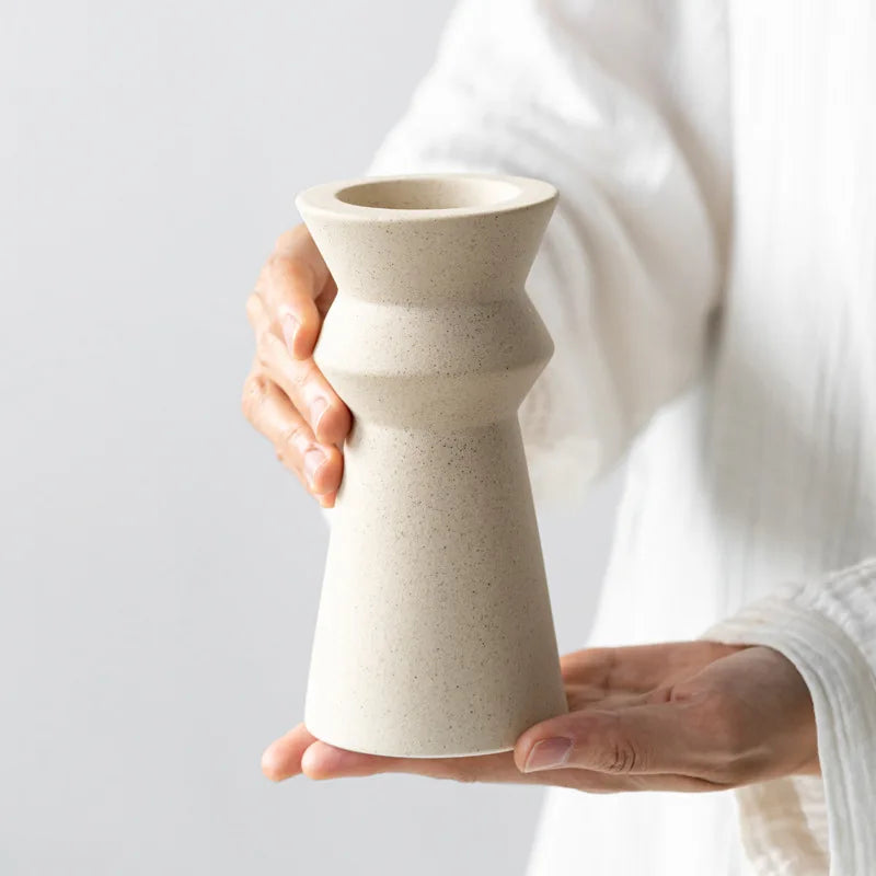 Hands holding white ceramic candle holder on light neutral background