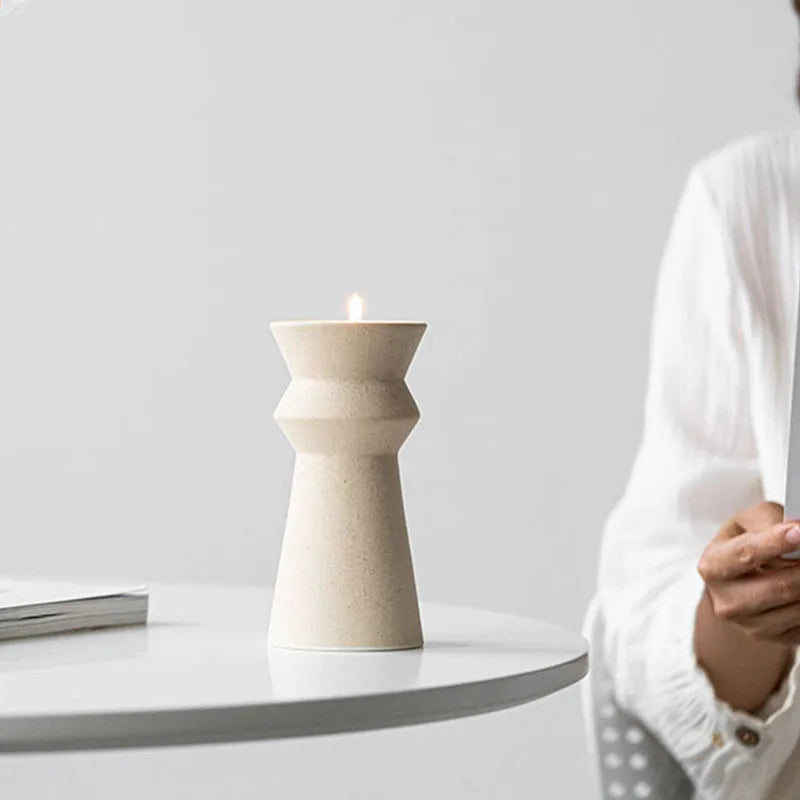 Hands holding white ceramic candle holder on light neutral background