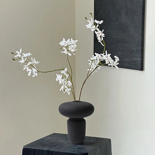 Black textured ceramic vase on black wooden stool and white flower branch