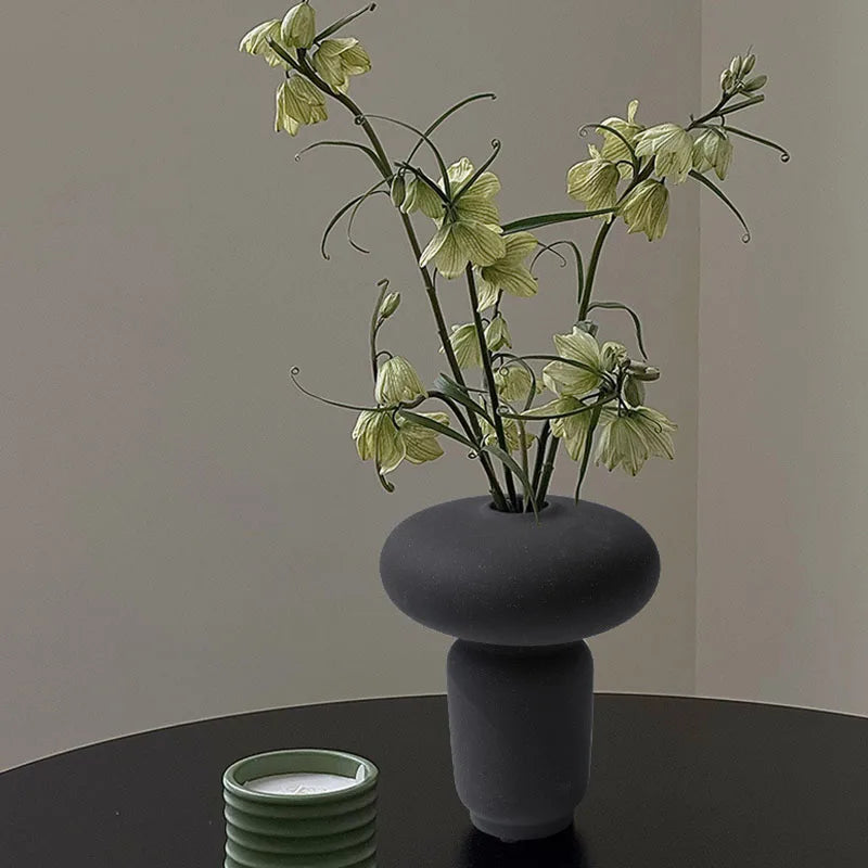 Black textured ceramic vase on black table and green flowers