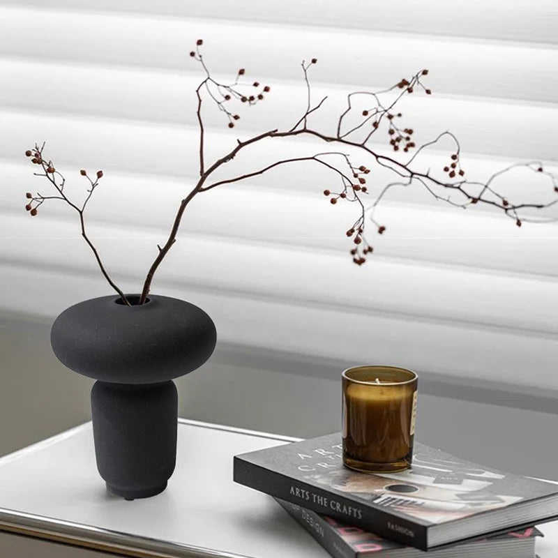 Black textured ceramic vase with branch and books on bright room background