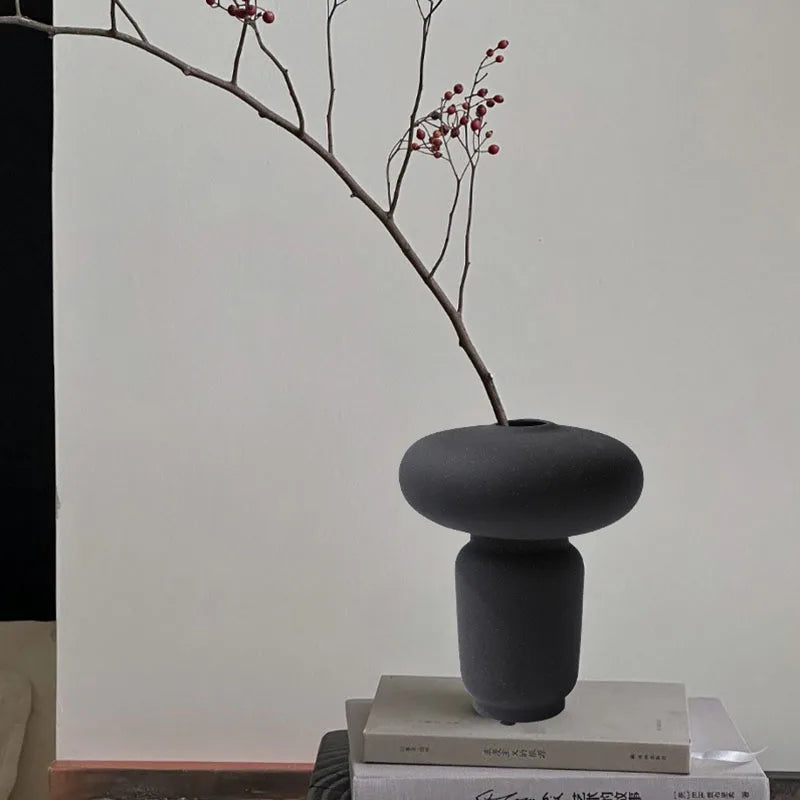 Black textured ceramic vase with branch and books on bright room background