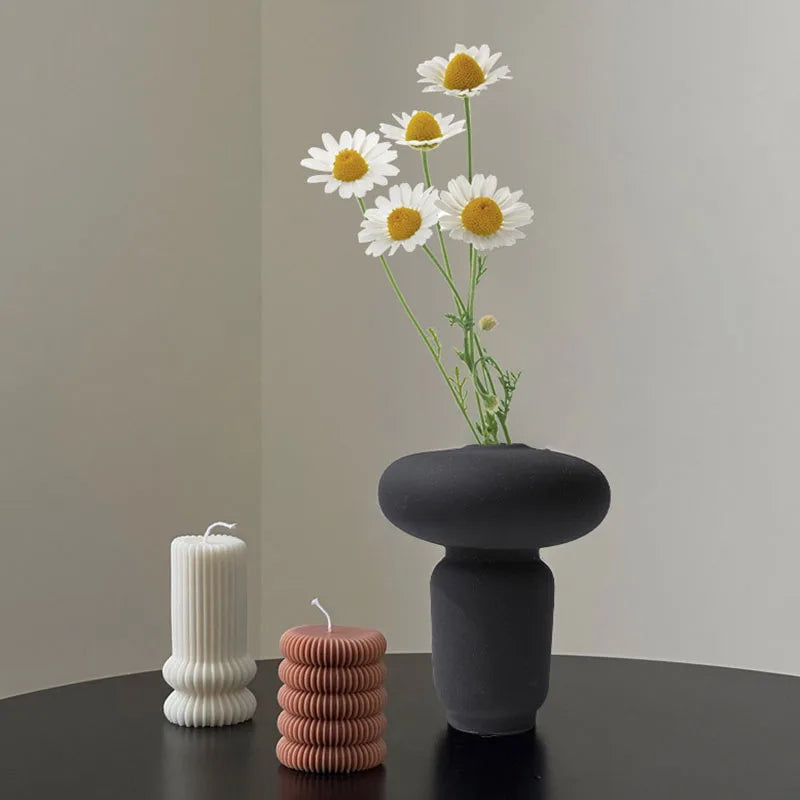 Black textured ceramic vase on black table, candles and white flowers