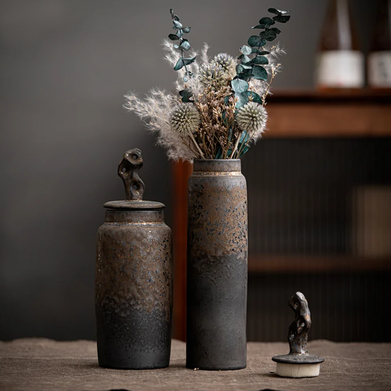 Set of two tall, dark grey ceramic storage jars with bronze accents on japanese tray and dark room background