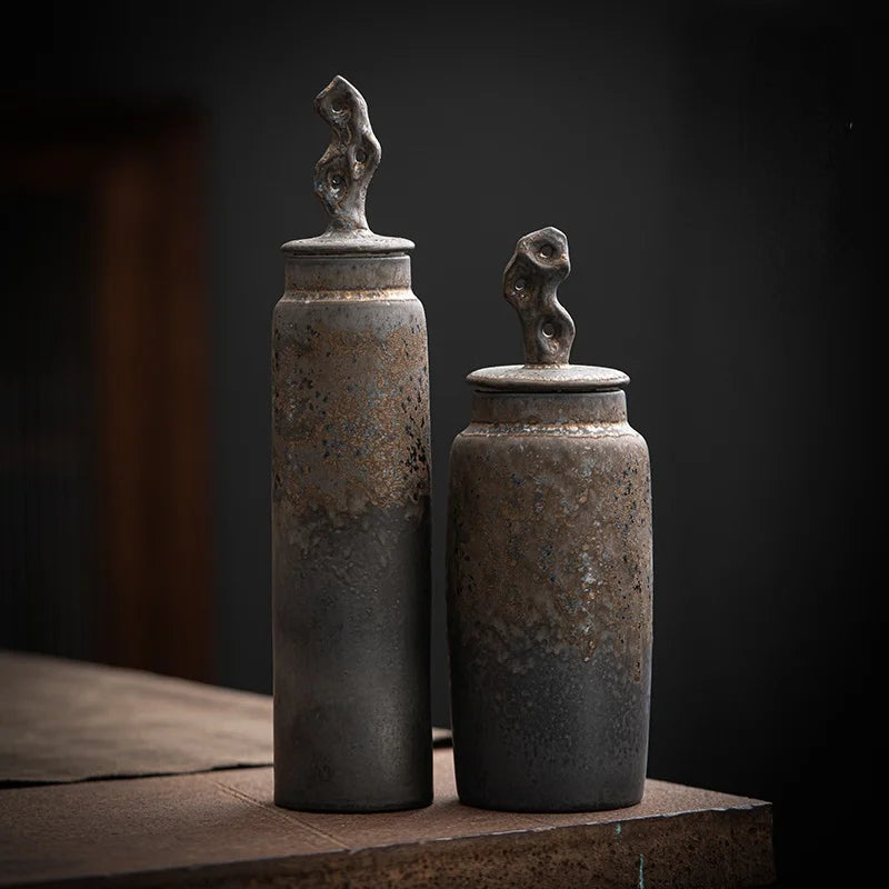 Set of two tall, dark grey ceramic storage jar with bronze accents on dark neutral background