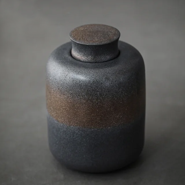 Dark grey ceramic storage jar with bronze accents on dark neutral background