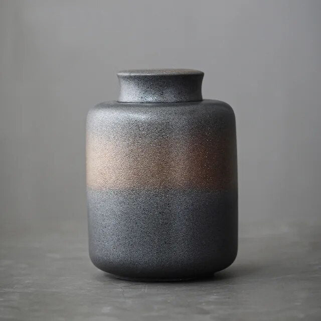 Dark grey ceramic storage jar with bronze accents on grey neutral background