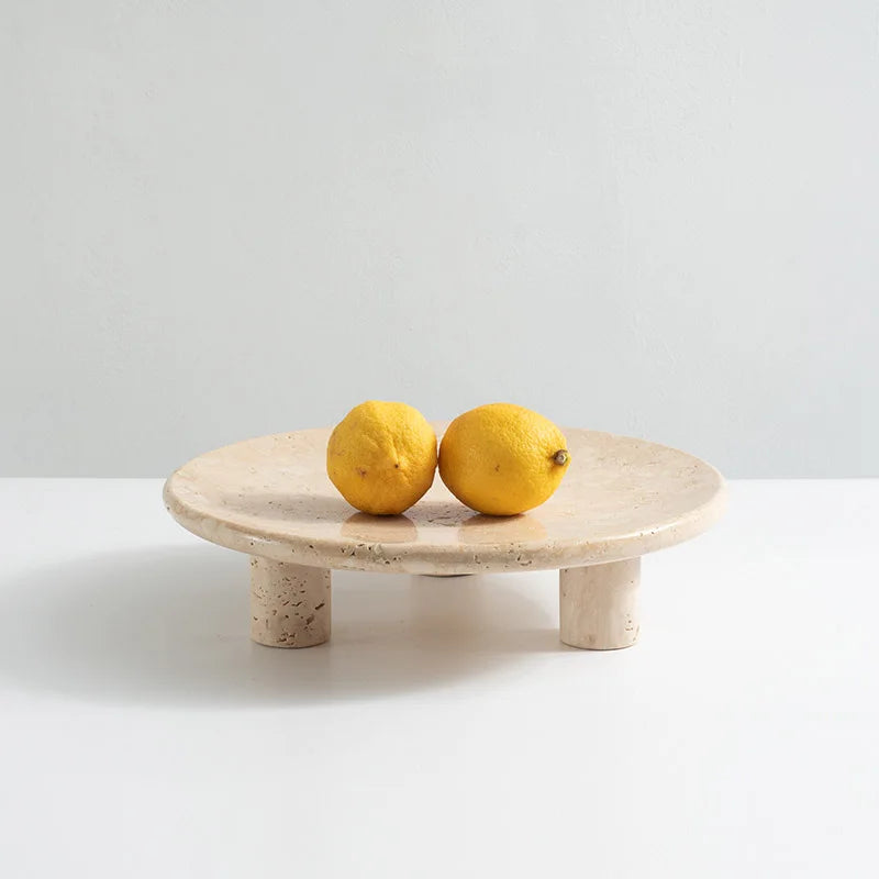 Two lemons on travertine round tray with three cylindrical feet on neutral background