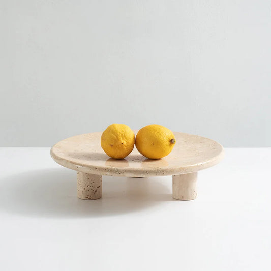 Two lemons on travertine round tray with three cylindrical feet on neutral background