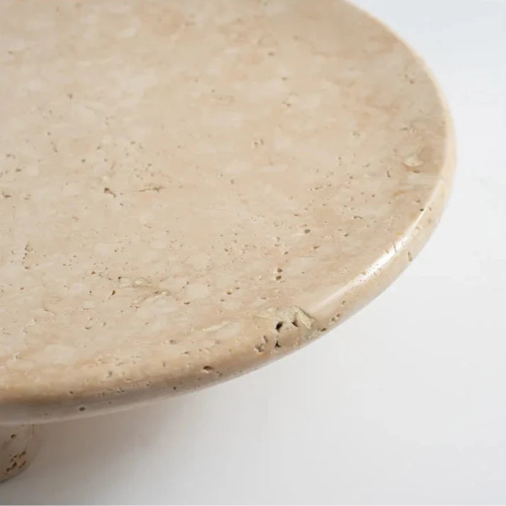 Detail of travertine round tray with three cylindrical feet on neutral background