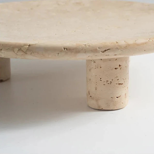 Detail of travertine round tray with three cylindrical feet on neutral background