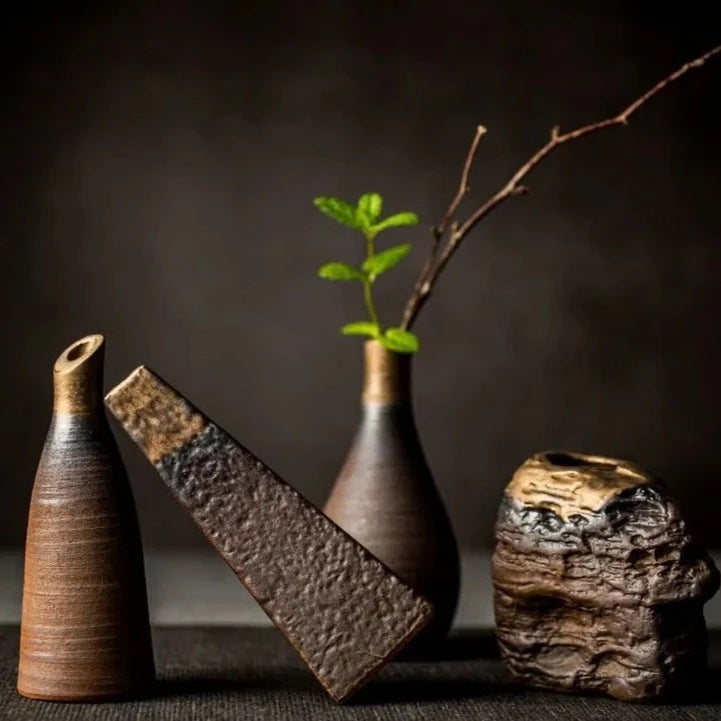 Composition of dark grey textured ceramic vases with bronze accents and different shapes, on dark neutral background
