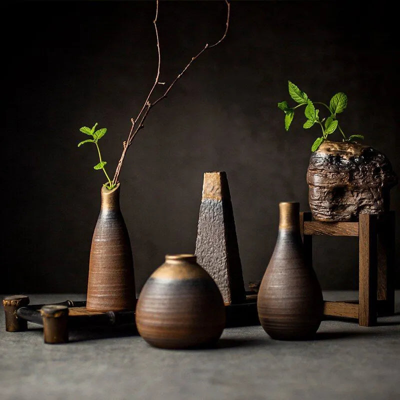 Composition of dark grey textured ceramic vases with bronze accents and different shapes, on dark neutral background