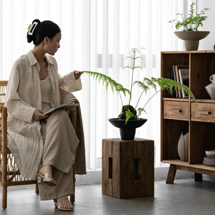 Woman sitting close to handcrafted rectangular wooden side table with black vase and plant in japandi living room