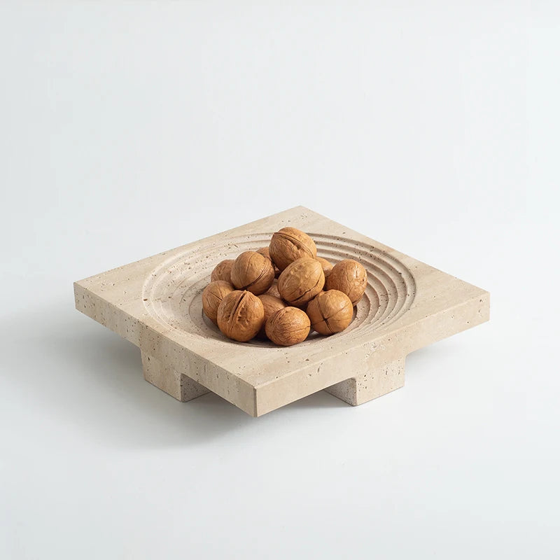 Walnuts in travertine round tray with concentric decoration and elevated base, on neutral background