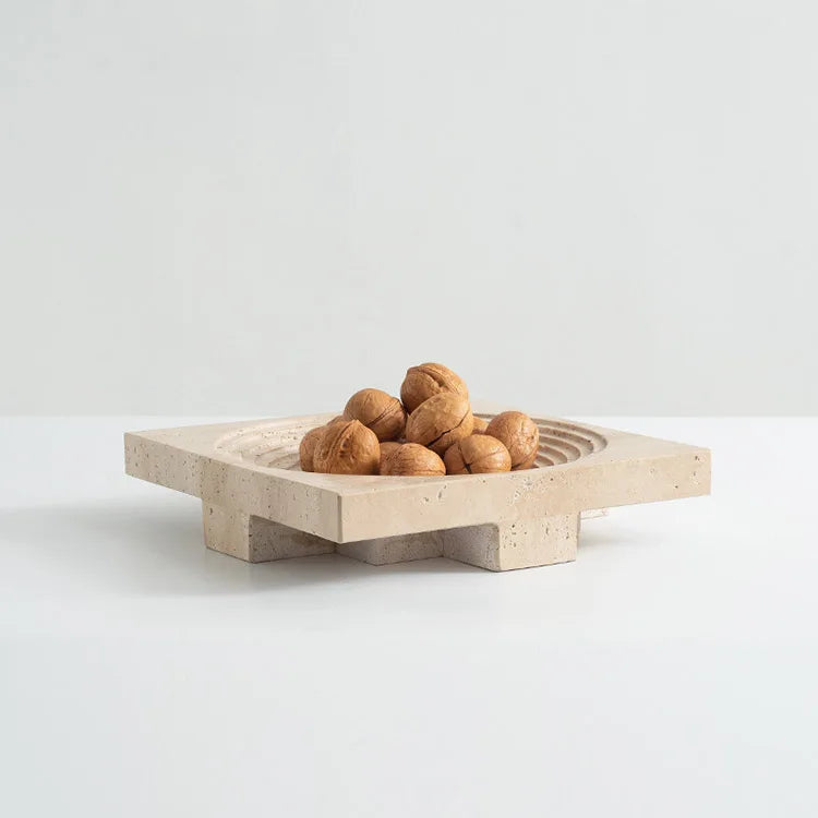 Walnuts in travertine round tray with concentric decoration and elevated base, on neutral background
