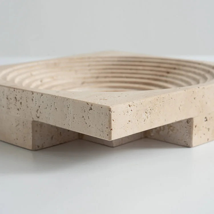 Detail of square travertine round tray with concentric decoration and elevated base, on neutral background