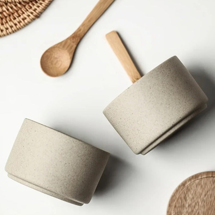 Profile view of two grey ceramic spice jars with wooden lids and wooden spoons on bright kitchen countertop