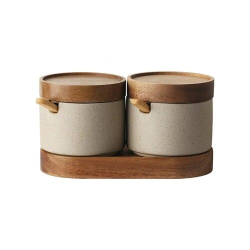 Set of two grey ceramic spice jars with wooden lids, wooden spoons and oval wooden tray on white background