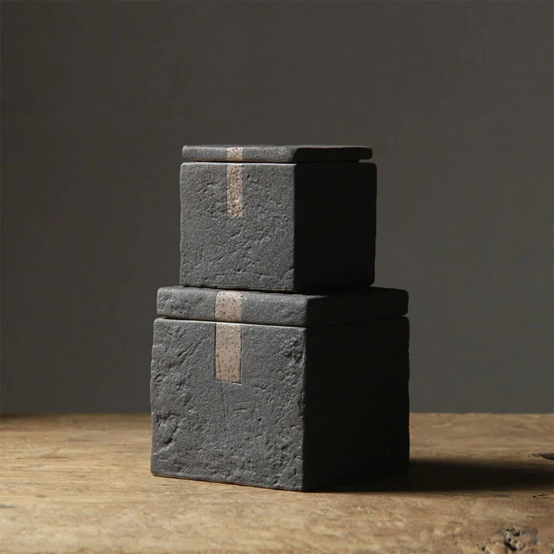 Set of two dark grey textured square ceramic jars with decorative accent on dark neutral background