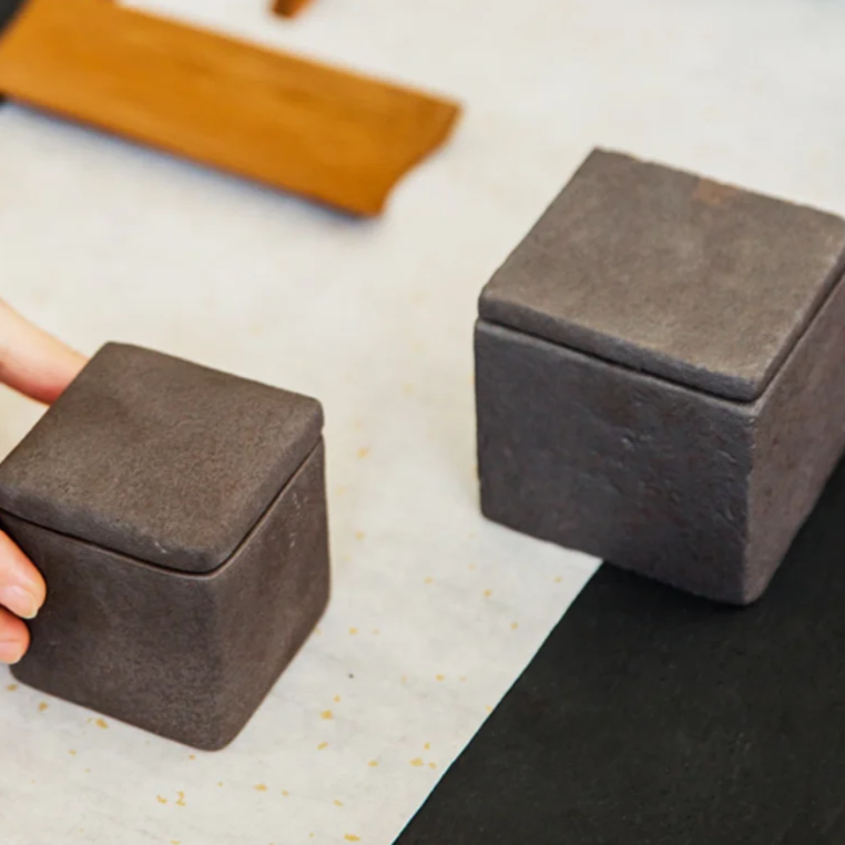 Set of two japandi dark grey textured square ceramic jars with decorative accent on dark neutral background