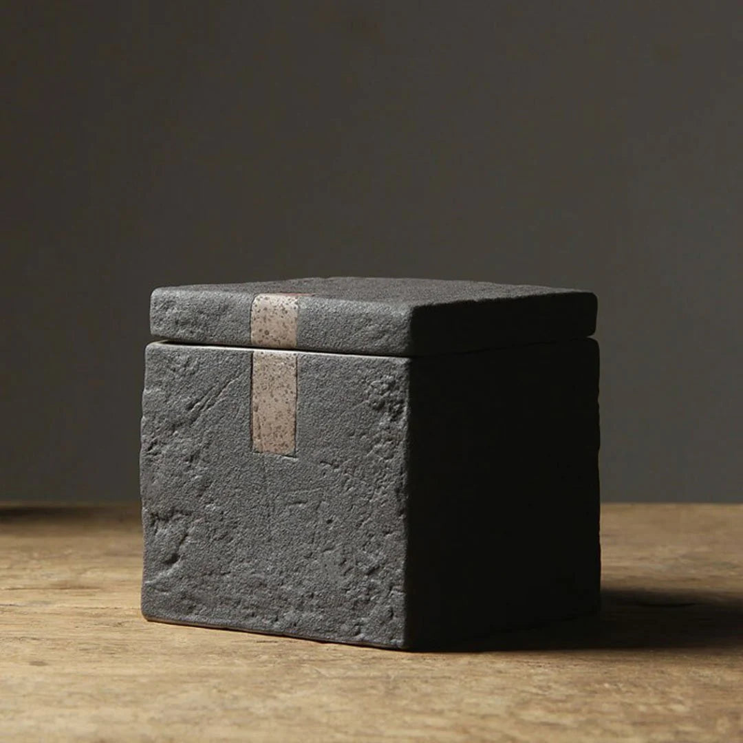 Dark grey textured square ceramic jar with decorative accent on dark neutral background