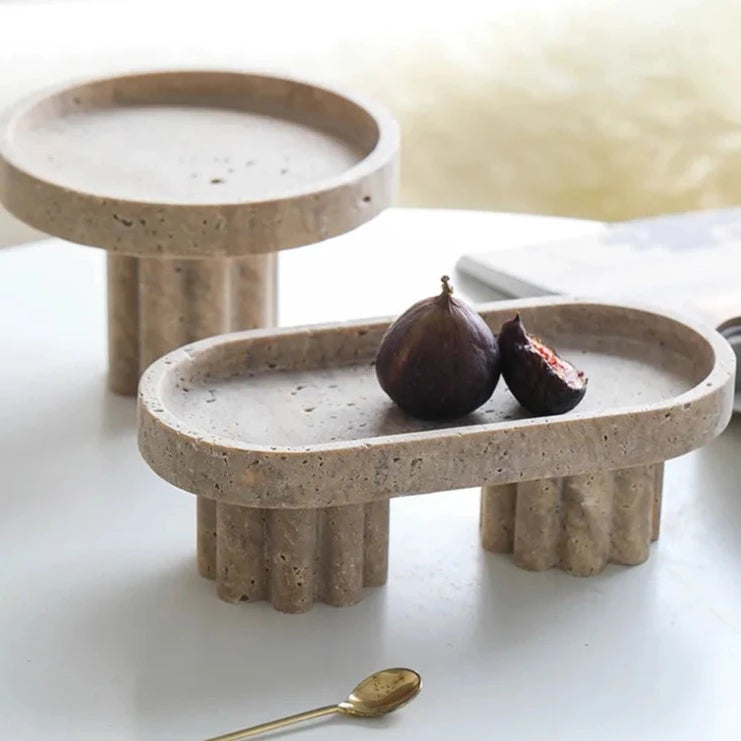 Two travertine trays with scalloped stands in neutral room