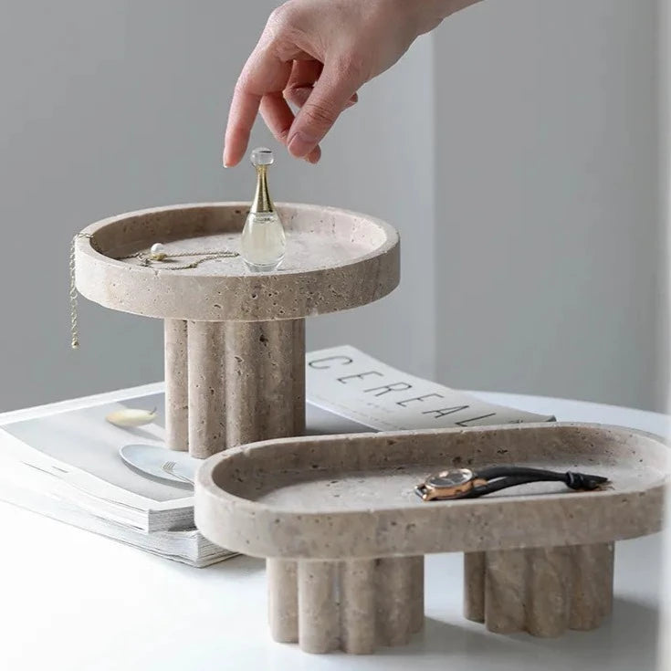 Two travertine trays with scalloped stands in neutral room