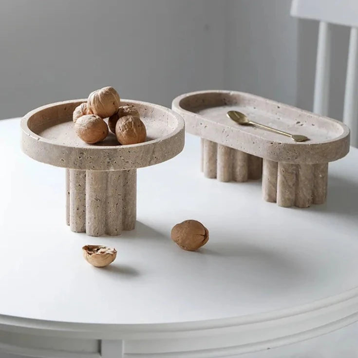 Two travertine trays with scalloped stands in neutral room