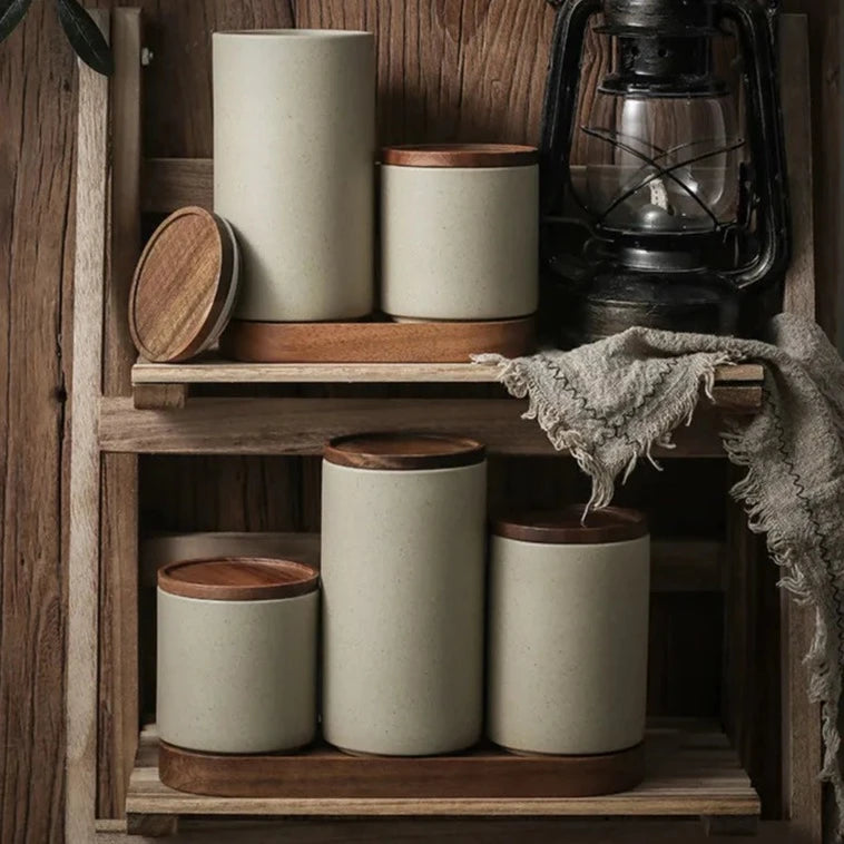 Set of grey ceramic spice jars with wooden lids and oval wooden tray on wooden shelf