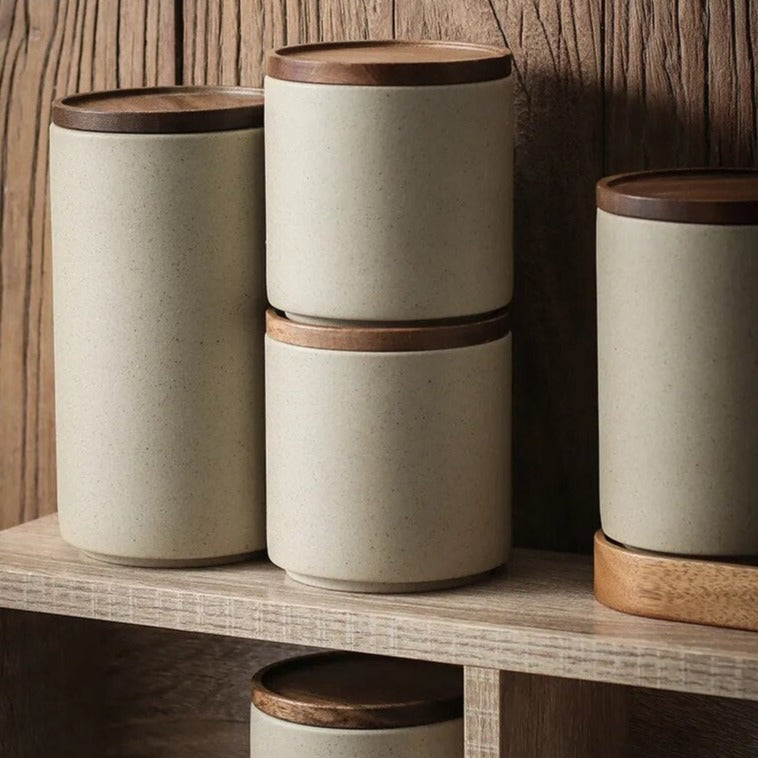 Set of grey, stacking ceramic spice jars with wooden lids and oval wooden tray on wooden shelf