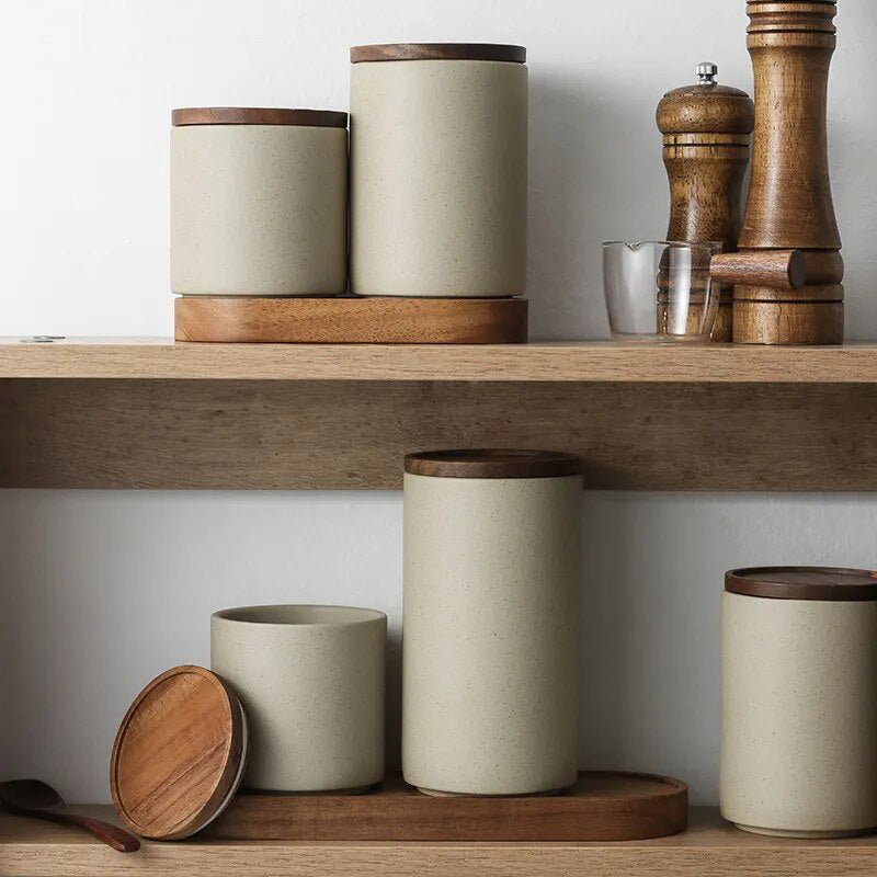 Set of grey ceramic spice jars with wooden lids and oval wooden tray on wooden shelf