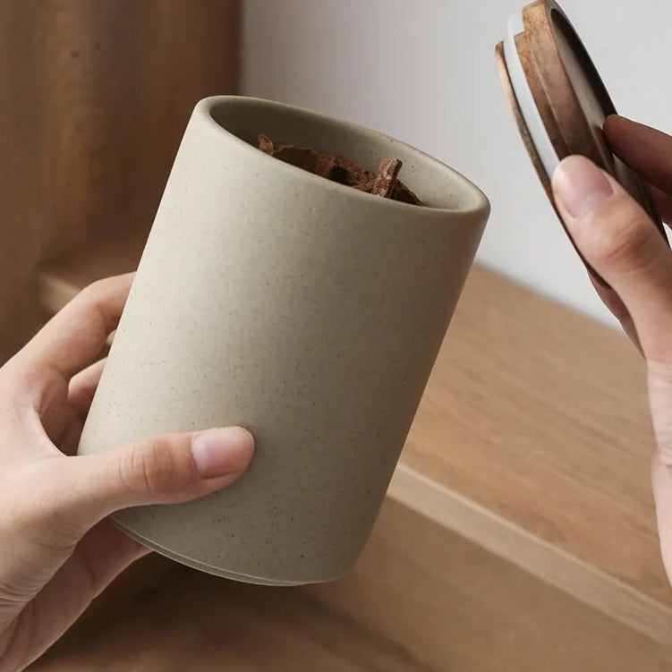 Woman's hands opening a grey ceramic spice jar with wooden lid, with wood shelf background